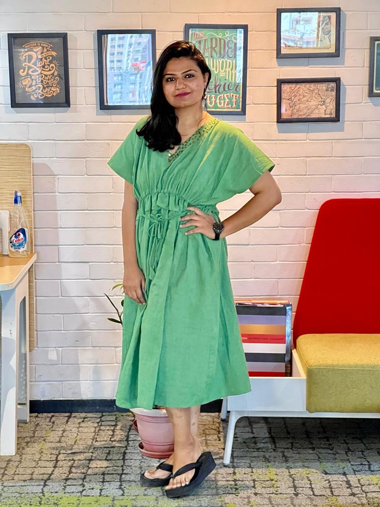 Woman in a green midi dress posing indoors with a stylish casual look against a cafe-style backdrop.