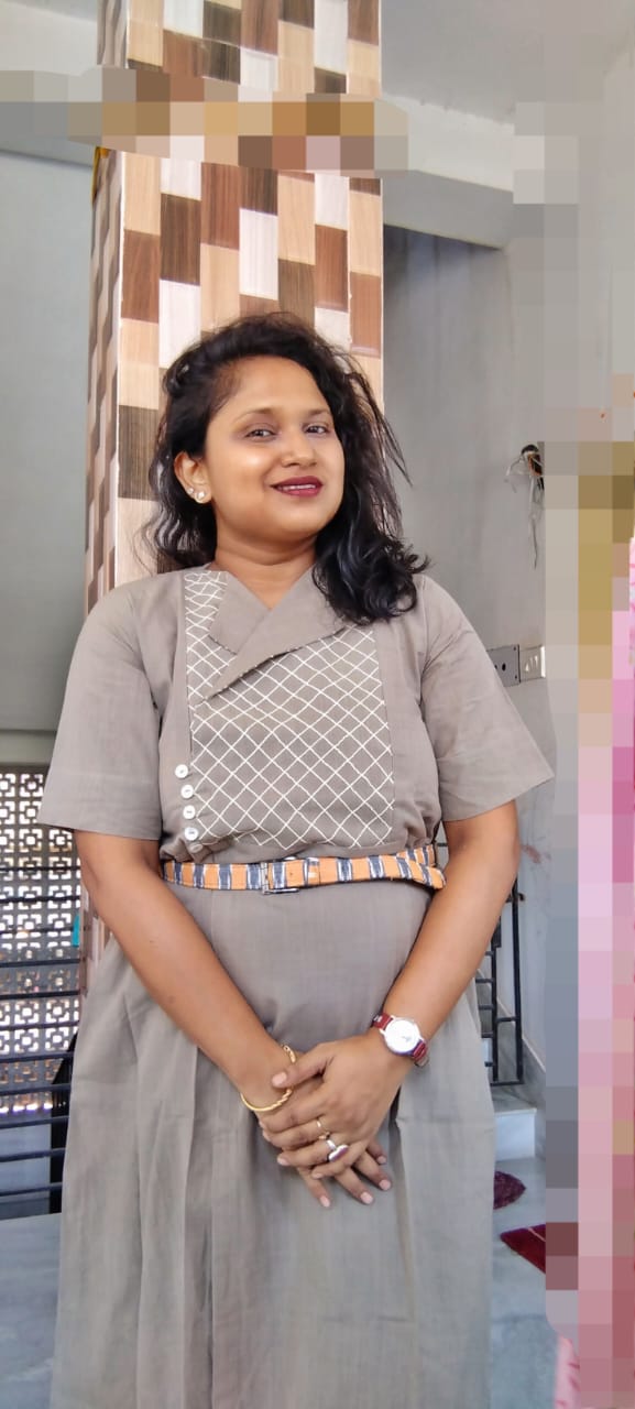 Woman in a grey dress with patterned detail and belt posing indoors with a stylish casual look.