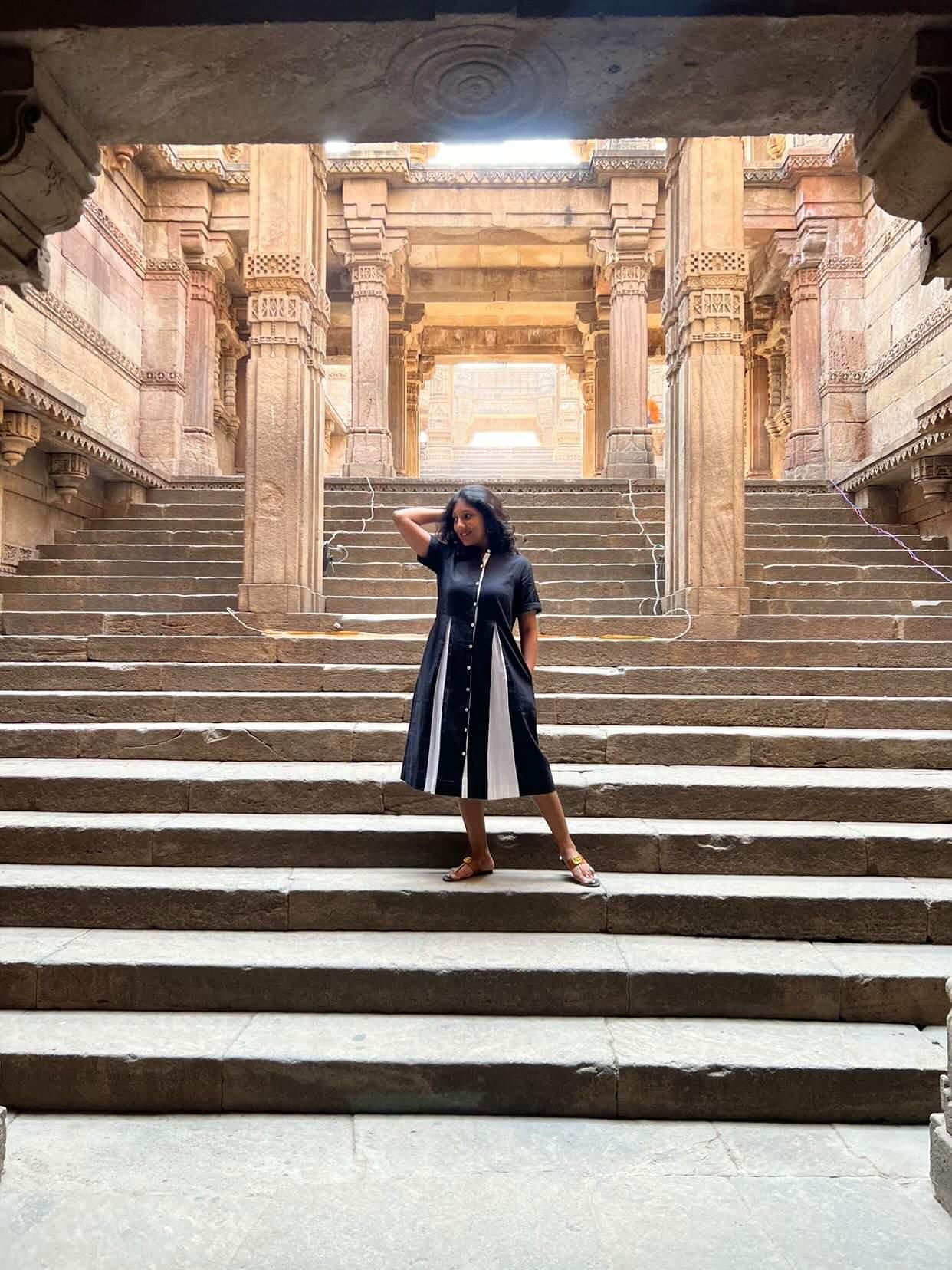 Woman in a black midi dress posing on stone steps inside a historic temple-style architecture.