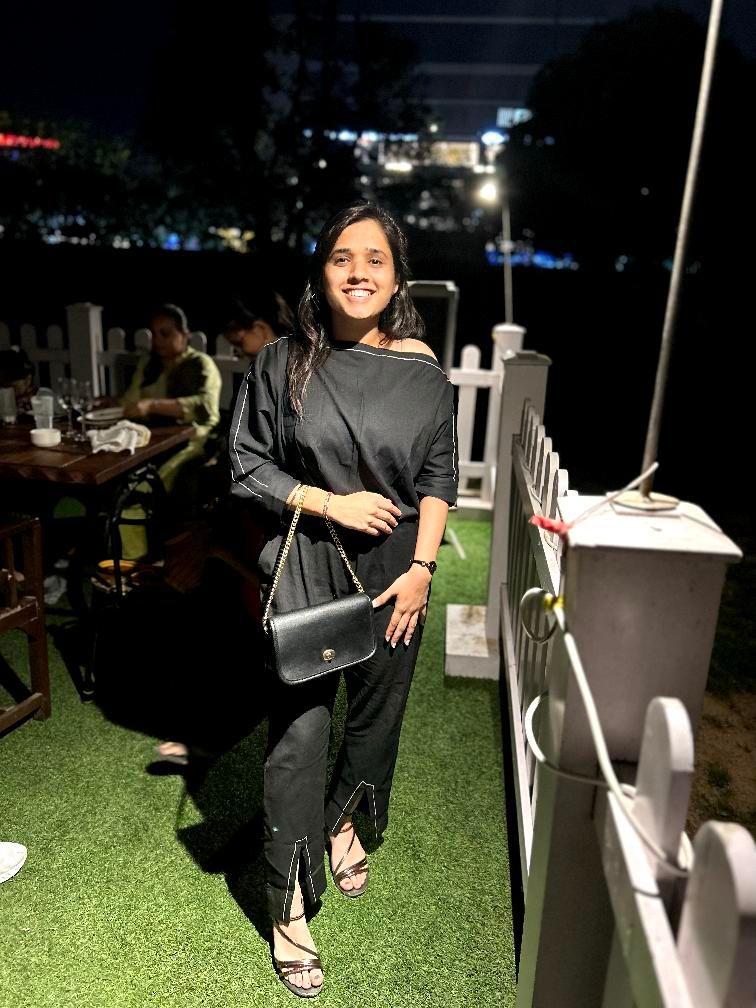 Woman in a black outfit posing outdoors at night with a stylish handbag and elegant casual look.