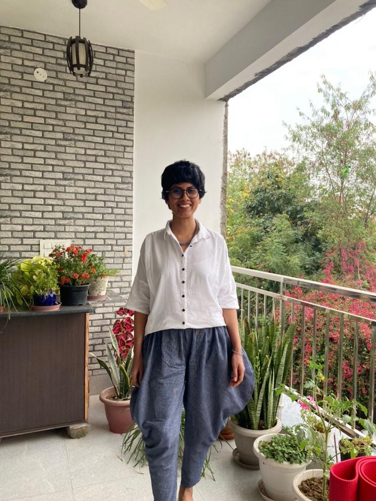 Woman in a white shirt and blue pants standing on a balcony surrounded by plants and greenery.