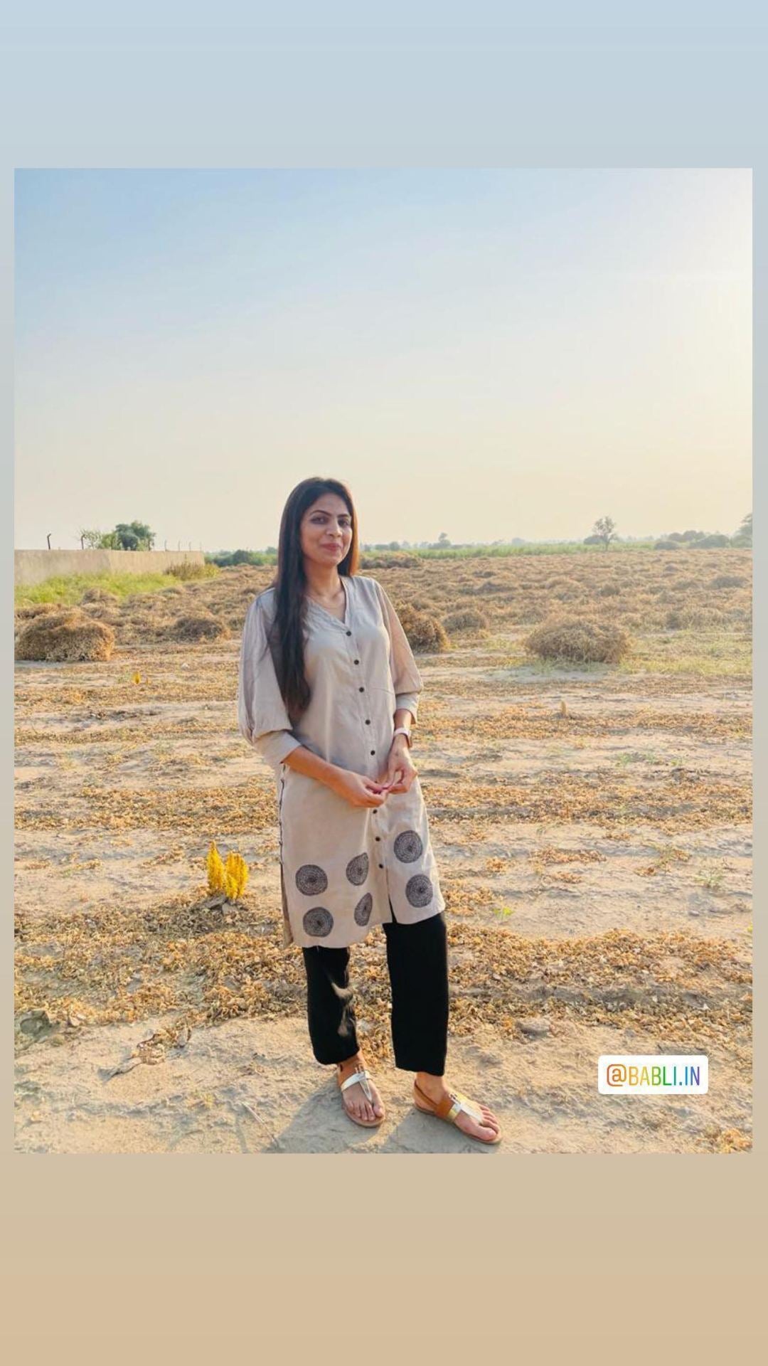 Woman in a beige printed kurta and black pants standing in an open field during sunset.