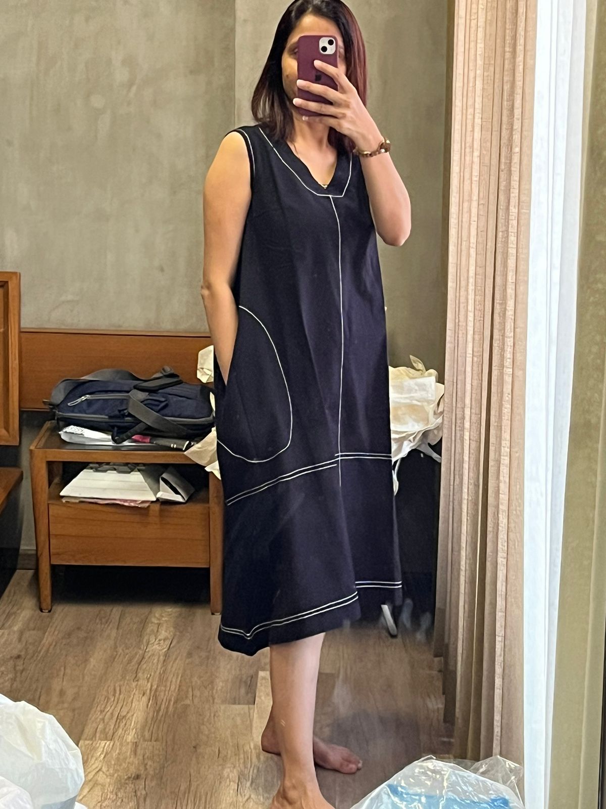 Woman taking a mirror selfie in a sleeveless black midi dress with contrast stitch detailing and pockets.