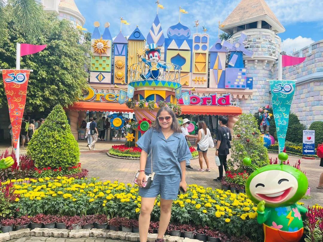 Woman posing in front of a colorful theme park entrance with floral decorations and cartoon characters.