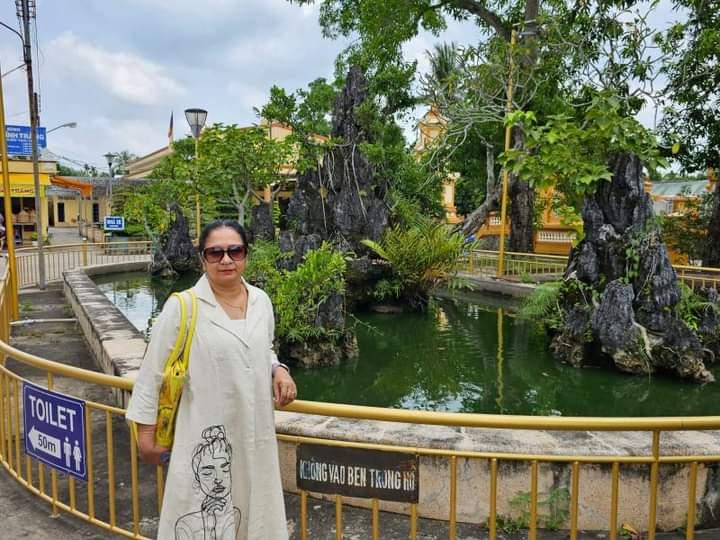 Woman standing near a scenic pond with rock garden and greenery at an outdoor tourist attraction.